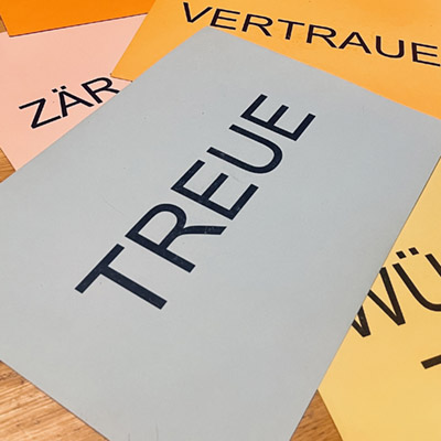 Bedruckte farbige Papierbögen. Auf dem obersten steht das Wort Treue.